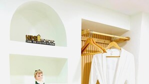 Ein weißer Raum mit einem Holzschrank, einem weißen Bademantel an einem hölzernen Kleiderbügel und einem gerahmten Bild auf einem Regal.