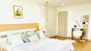 Ein modernes Schlafzimmer mit einem Holzkopfteil, einem großen Bett mit weißer Bettwäsche, einem Nachttisch mit Lampe sowie einem Schreibtisch mit Stuhl.