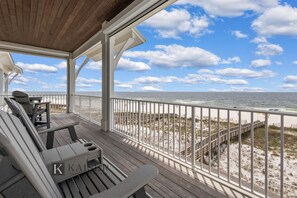 A wooden deck with Adirondack chairs and a view of the beach and ocean.