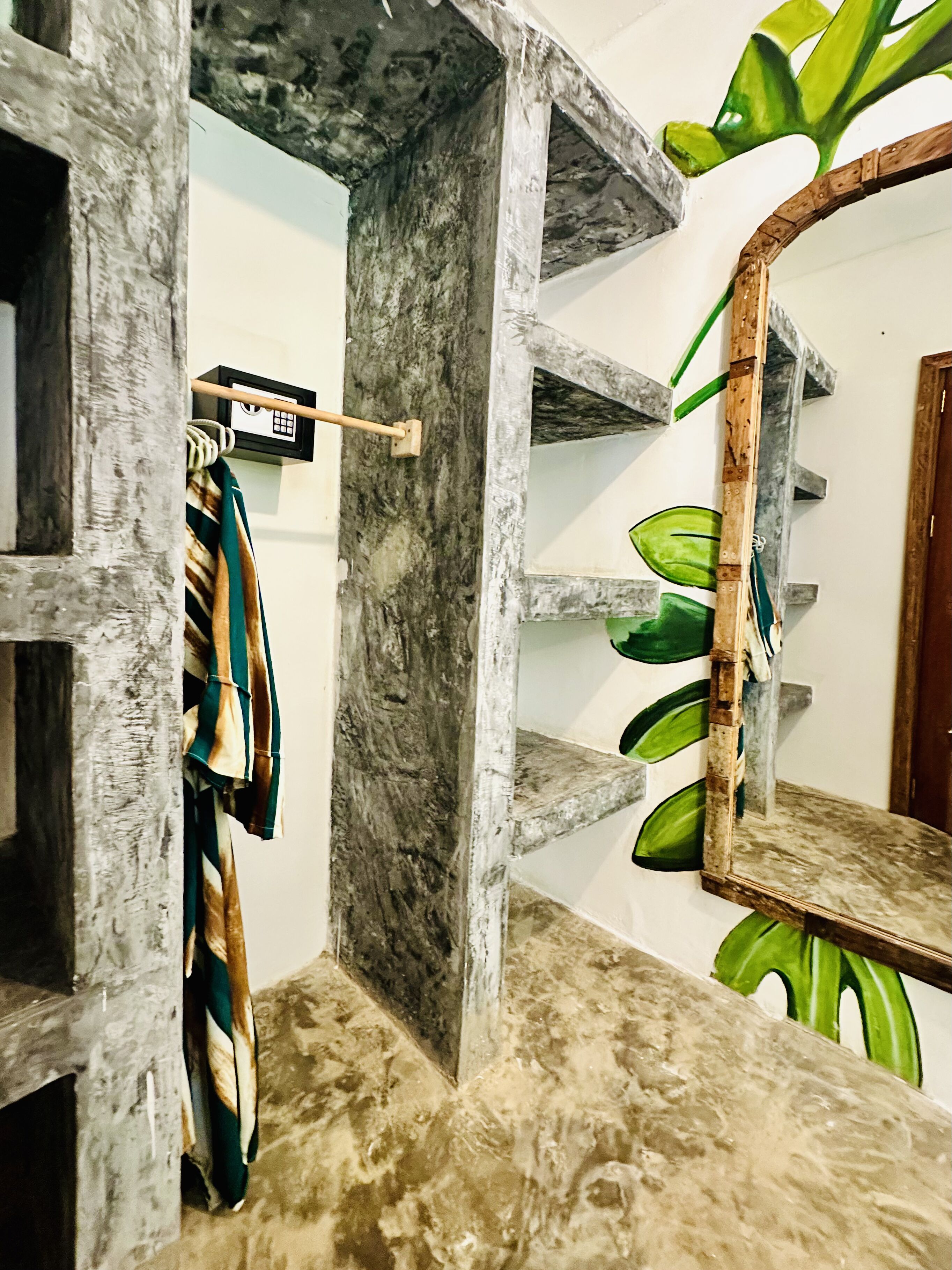 Quarto com piso de mármore, prateleira de madeira com desenho de folha verde e cabideiro com peça de roupa pendurada.