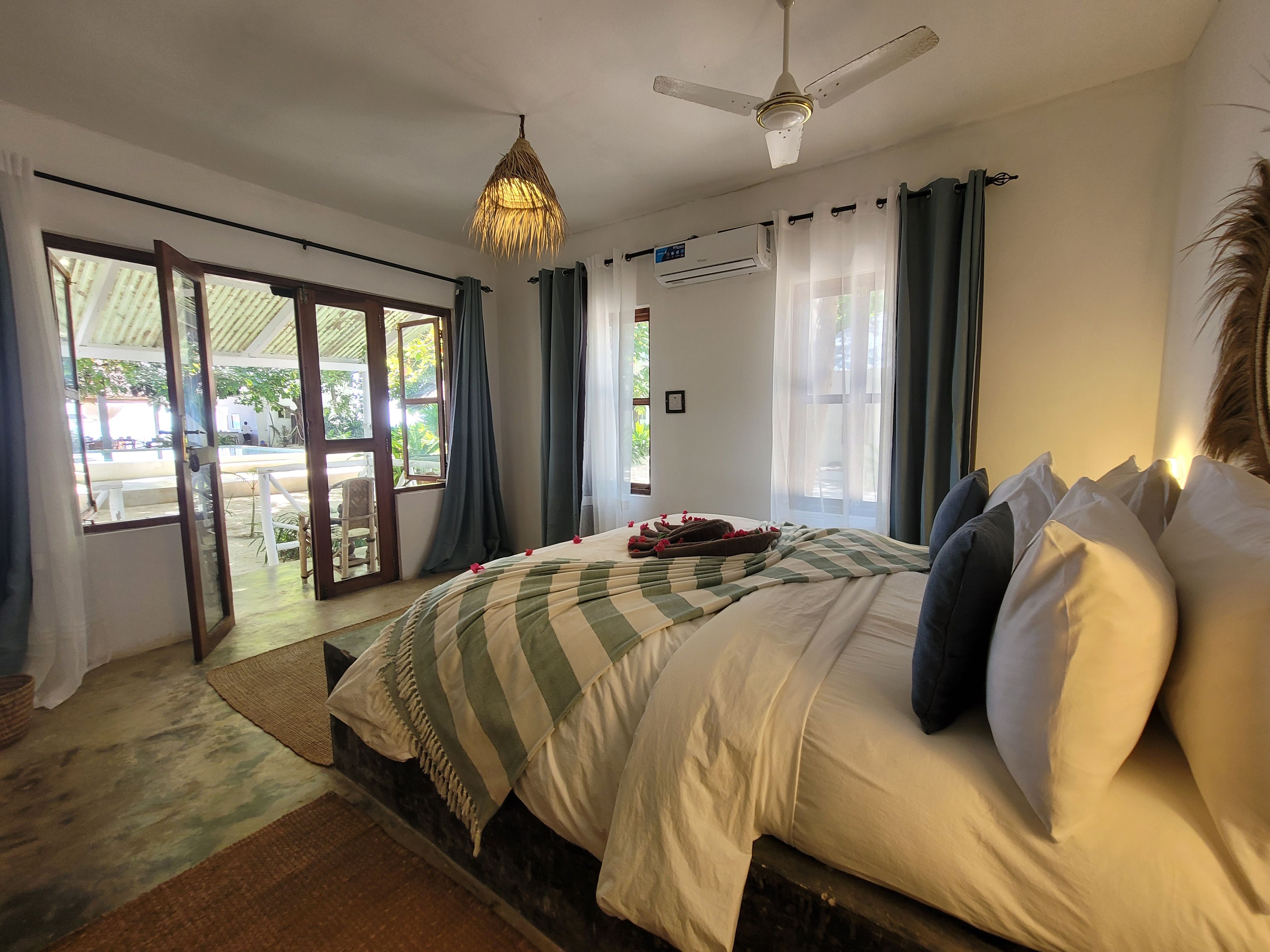 Een slaapkamer met een bed, een plafondventilator en uitzicht op buiten.