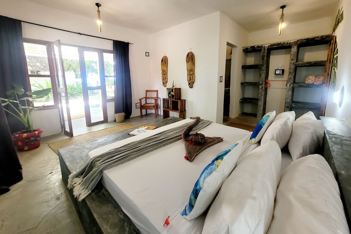 Habitació d'hotel amb un llit, una cadira, una taula petita i una prestatgeria amb sabates.