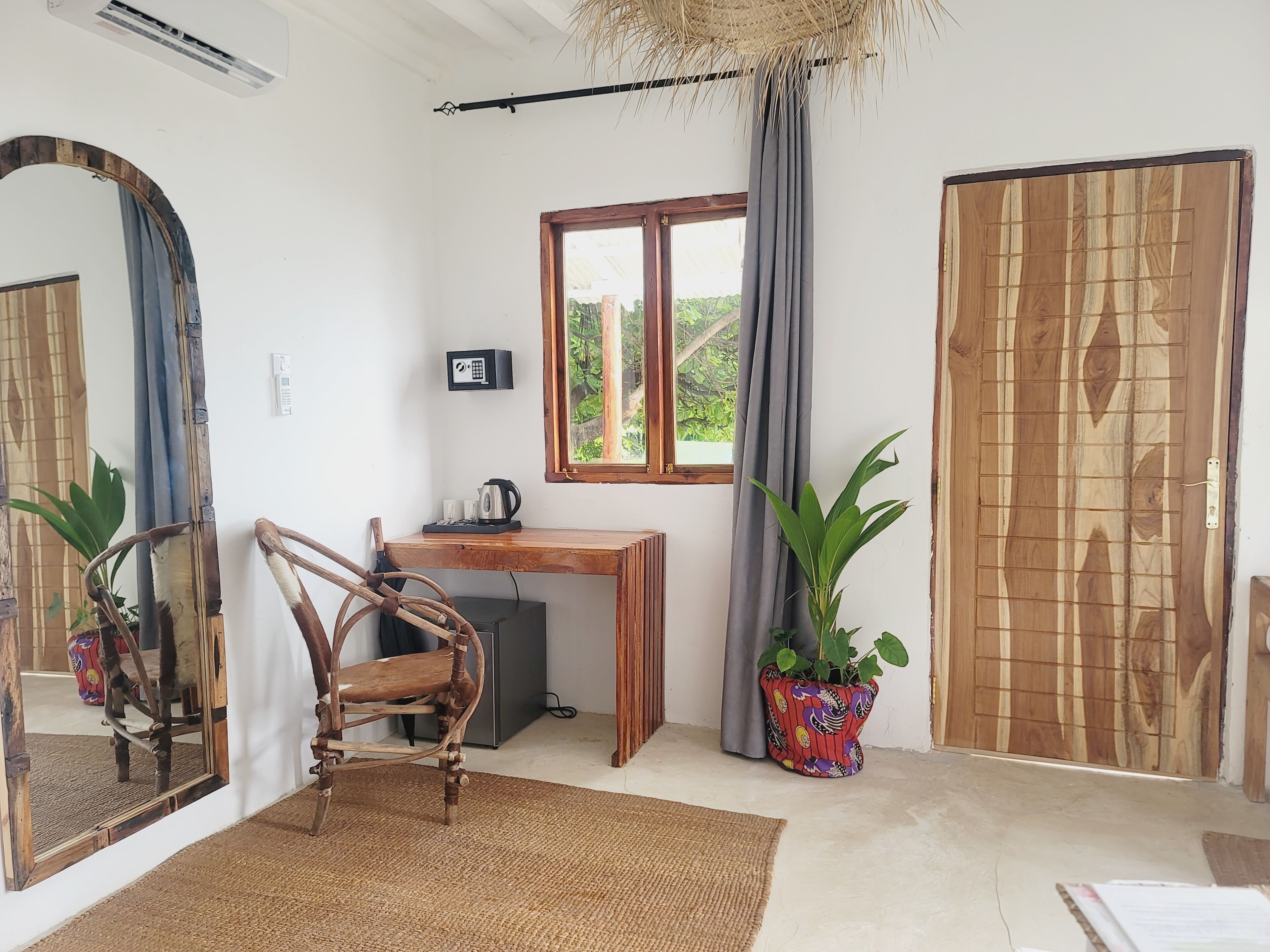 A room with a wooden desk, a chair, a potted plant, a large mirror, and a window with curtains.
