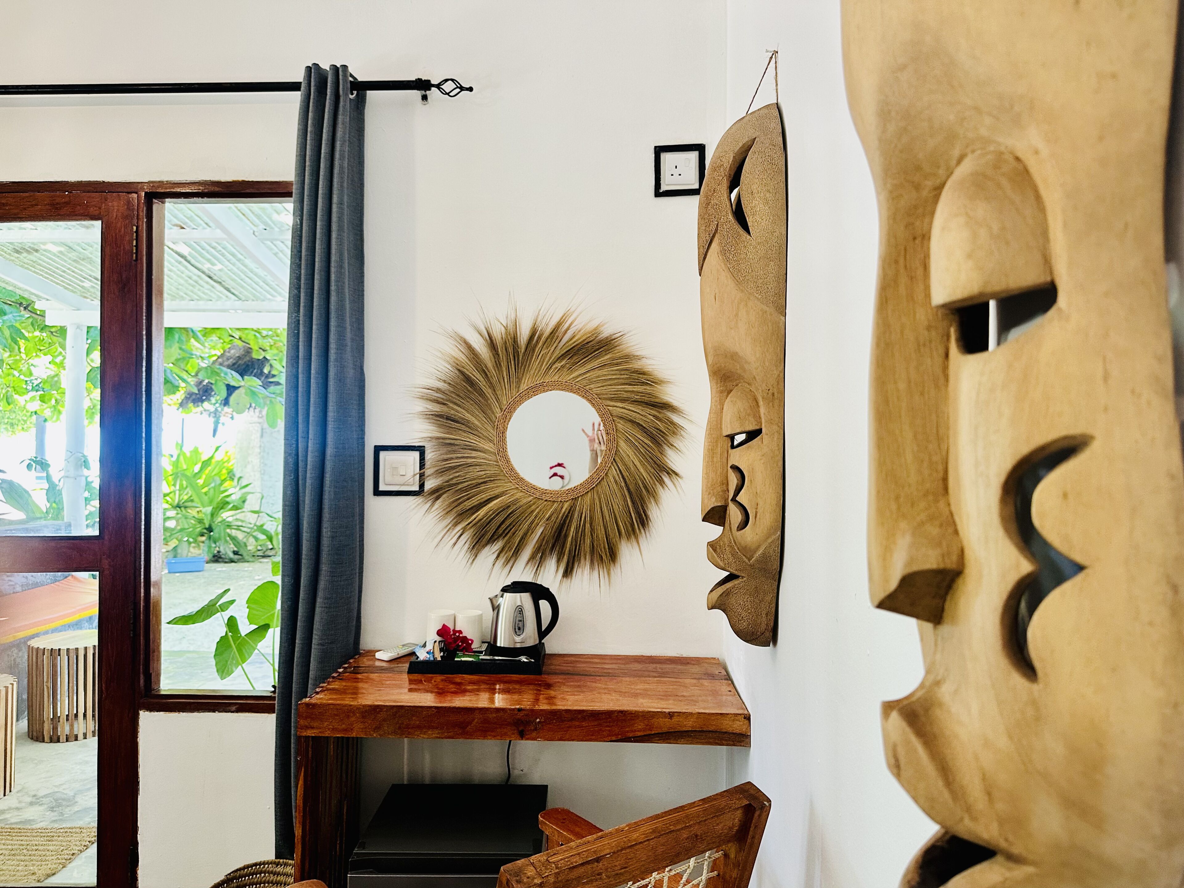 A room with a wooden table, a mirror, and a wooden mask on the wall.