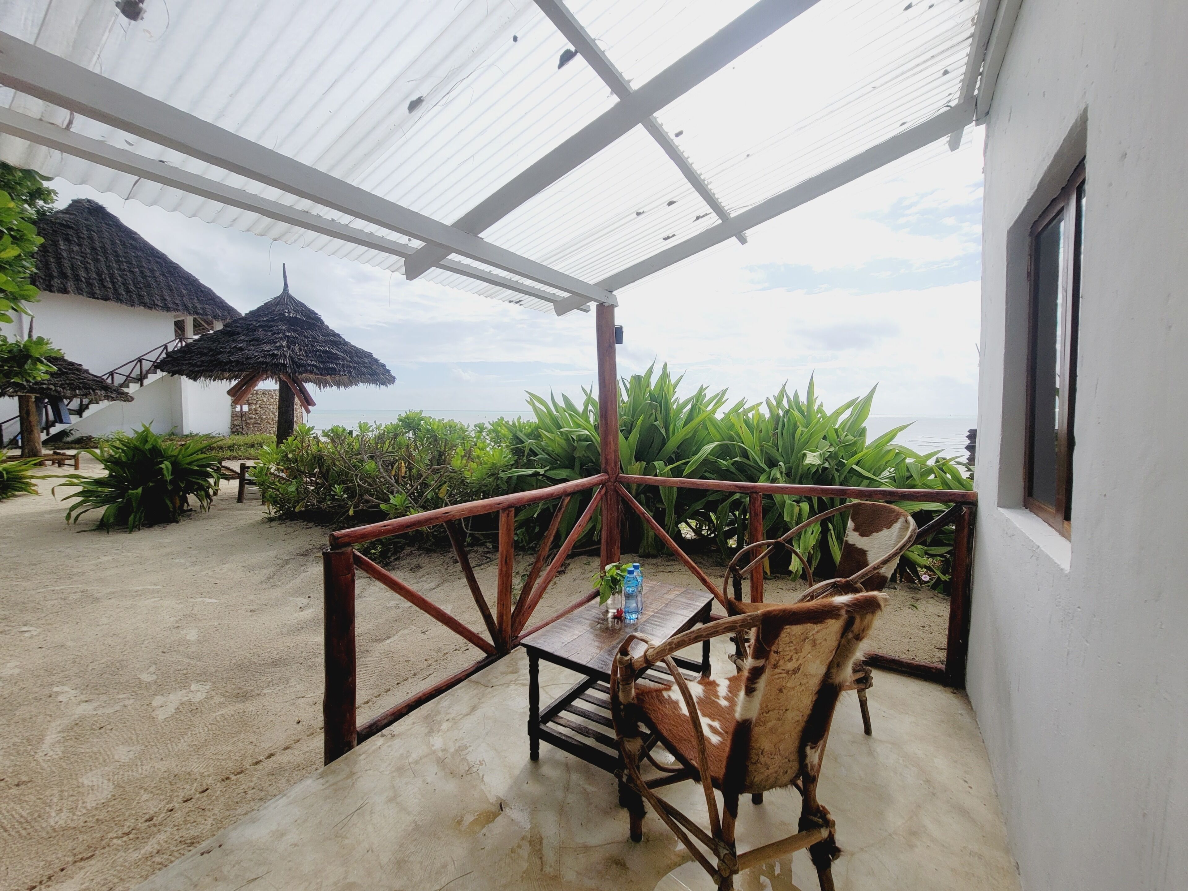 A covered outdoor area with a wooden chair, a table, and a thatched-roof structure.