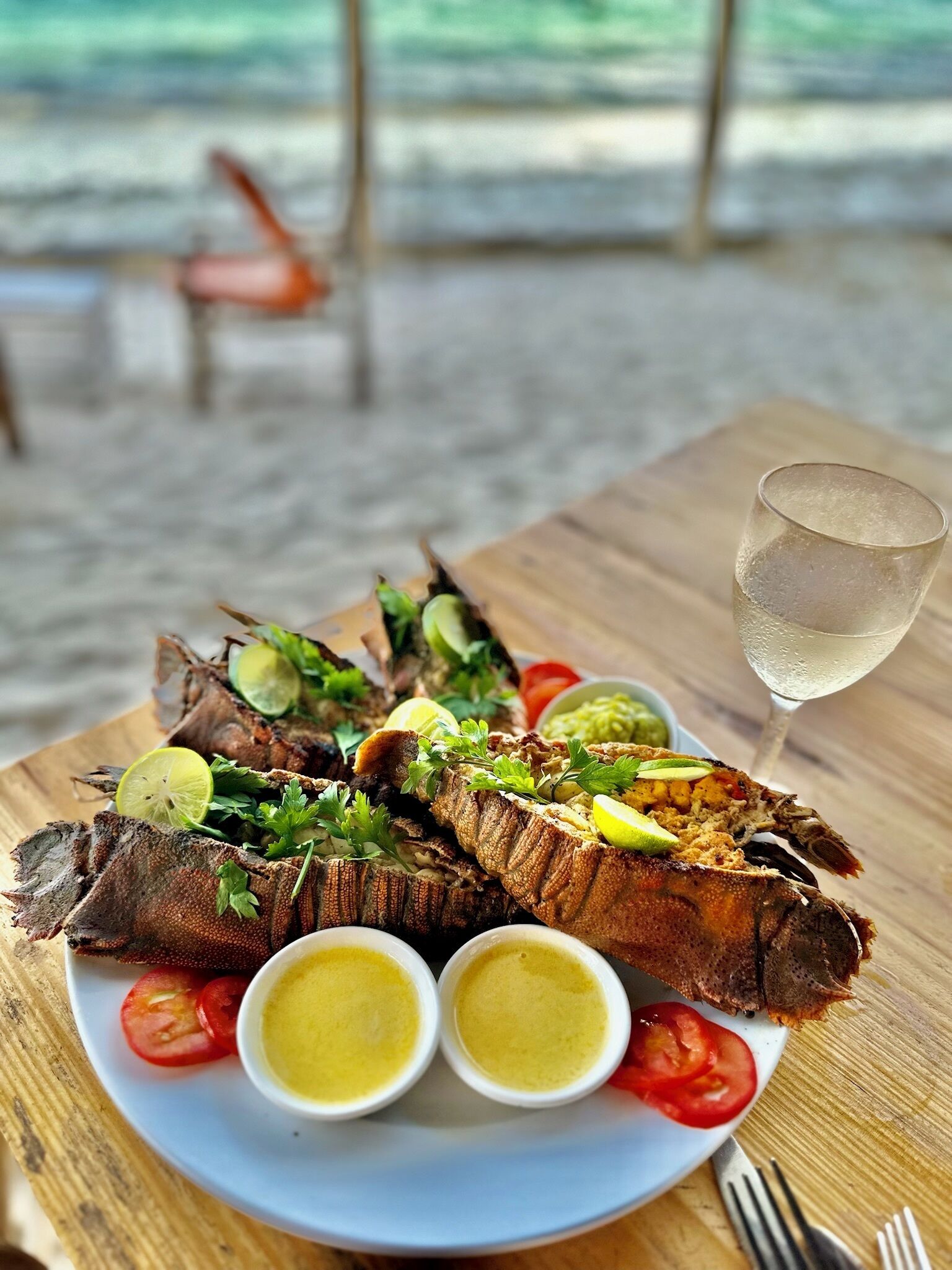 Un plat de fruits de mer agrémenté de tranches de citron et d’herbes aromatiques, accompagné de deux petits ramequins de sauce et d’un verre d’eau, le tout posé sur une table en bois.