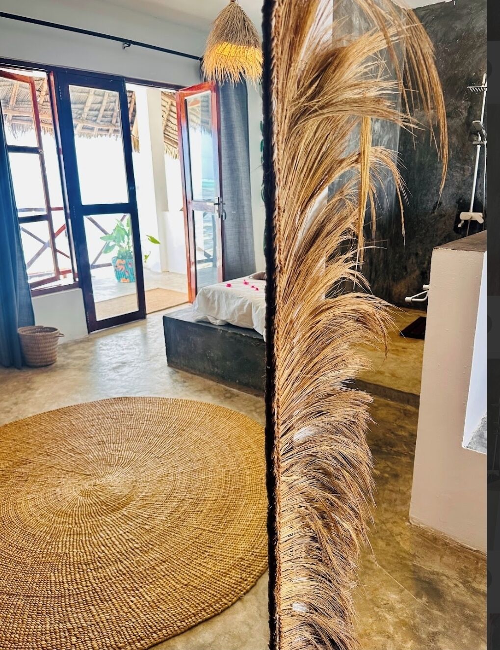 A room with a large woven rug, a feather decoration, and a view through a glass door.