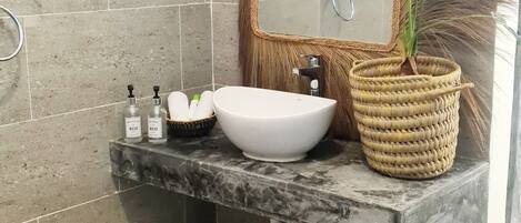A bathroom with a white sink, two bottles labeled 'ECO', a woven basket with a plant, and a mirror with a decorative frame.