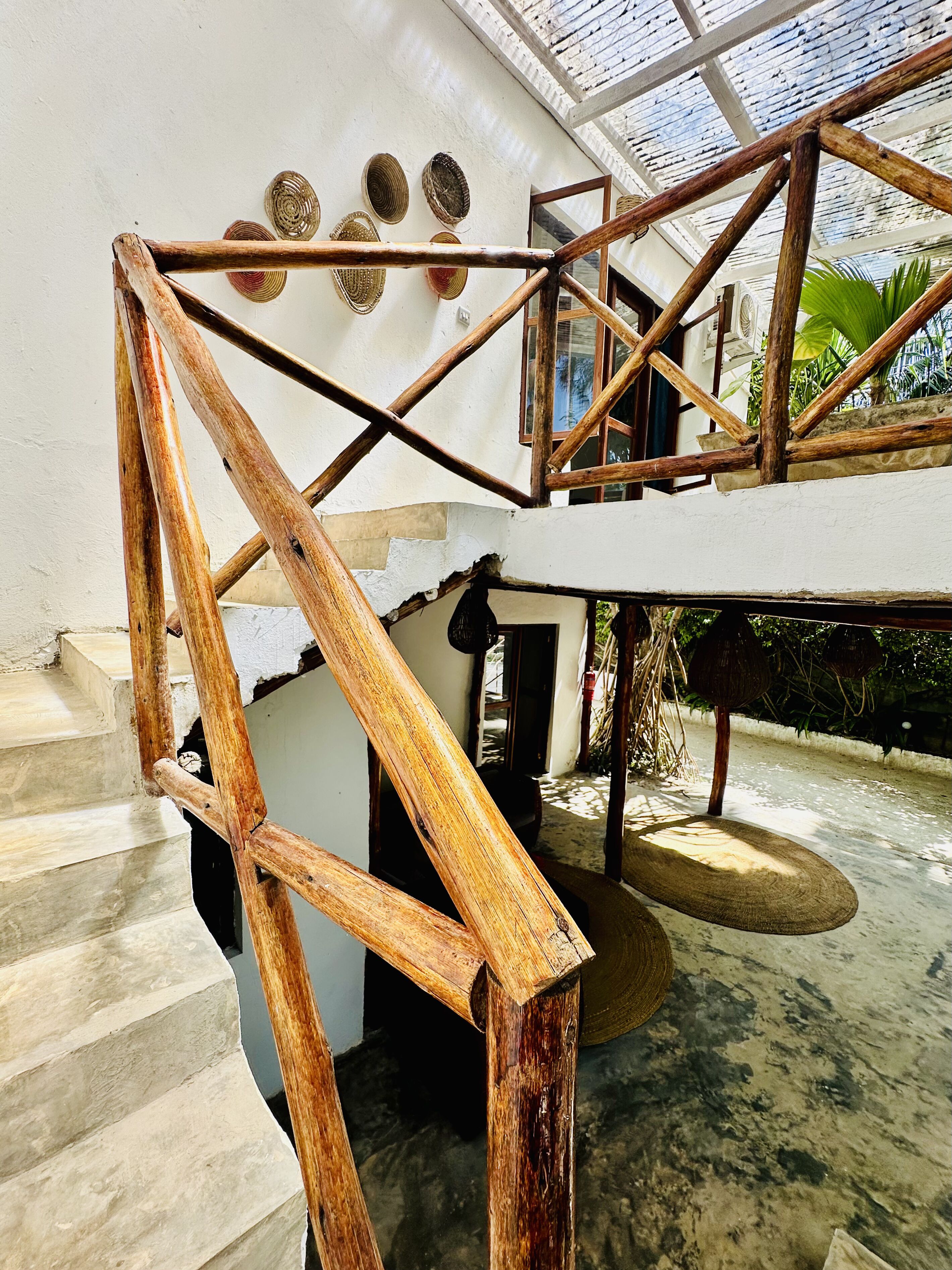A wooden staircase with a glass ceiling, a white wall with woven baskets, and a concrete floor.