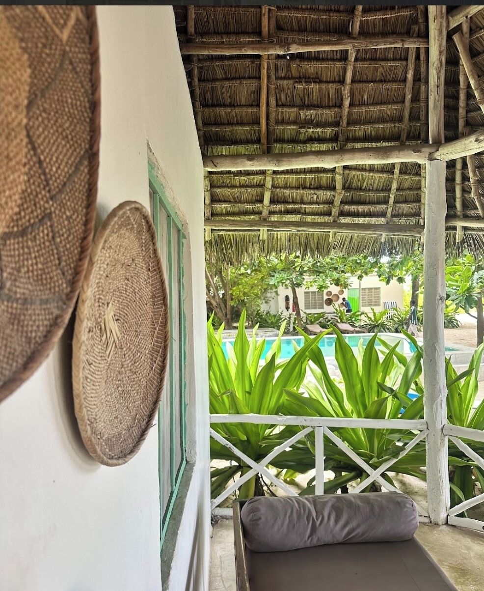 A covered outdoor seating area with a pool view, a hanging woven basket, and a white railing.