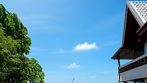 A paved road leading through a residential area with houses and greenery, under a clear blue sky. - Aksarai otel Patong  (Patong)