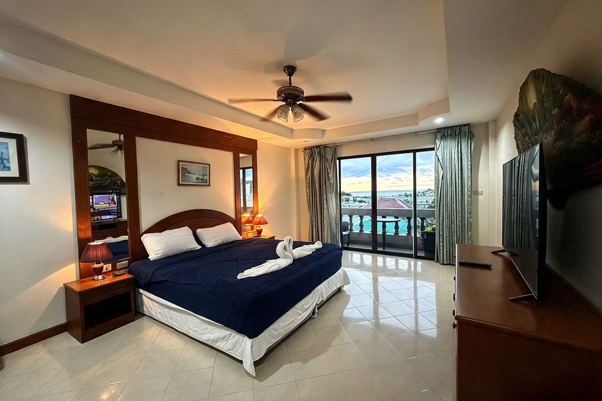 A hotel room with a bed, a ceiling fan, a television, and a view of the outside.