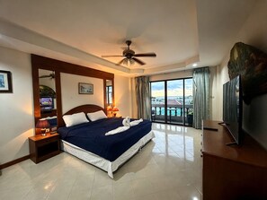 A hotel room with a bed, a ceiling fan, a television, and a view of the outside. - Aksarai otel Patong (Patong)