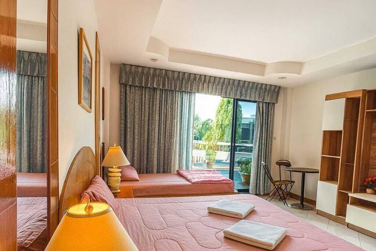 Una habitación de hotel con dos camas, un área de descanso con una mesa y sillas, un ventanal con cortinas y un espejo en la pared.