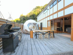 Une terrasse en bois avec un barbecue, une table et une structure en forme de dôme géodésique.