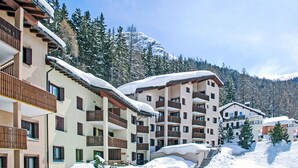 Un hôtel à plusieurs étages, doté de balcons, entouré d’arbres et de montagnes enneigées.