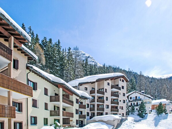 A multi-story hotel with balconies, surrounded by snow-covered trees and mountains.