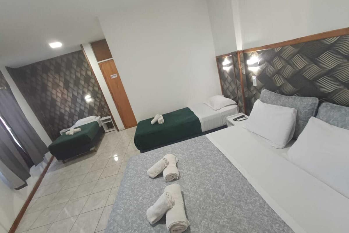 A hotel room with two single beds, a large bed, and a headboard with a geometric pattern.