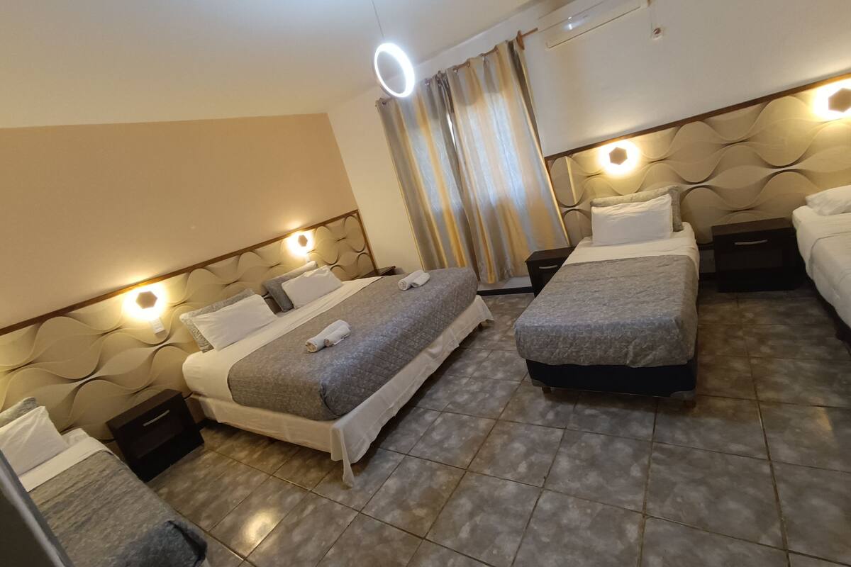 A hotel room with two beds, a nightstand, and a wall-mounted air conditioner.