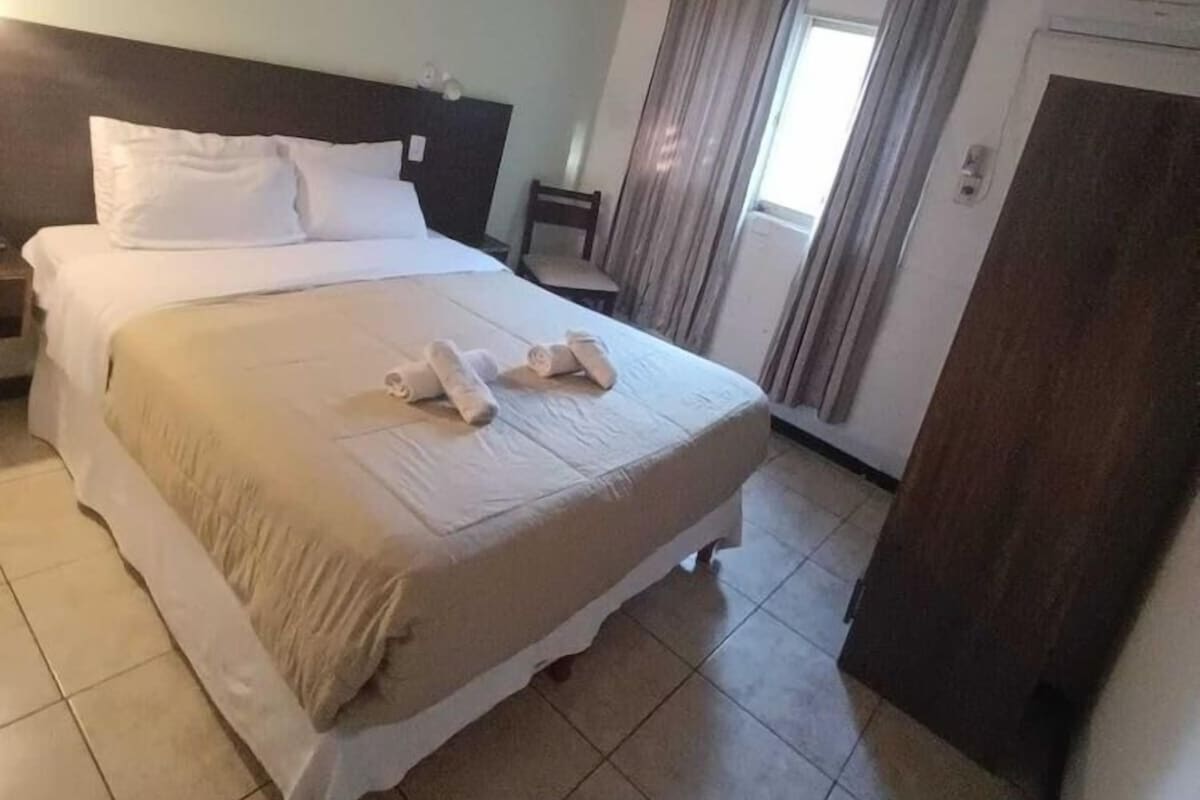 A hotel room with a bed, curtains, a chair, and a door.