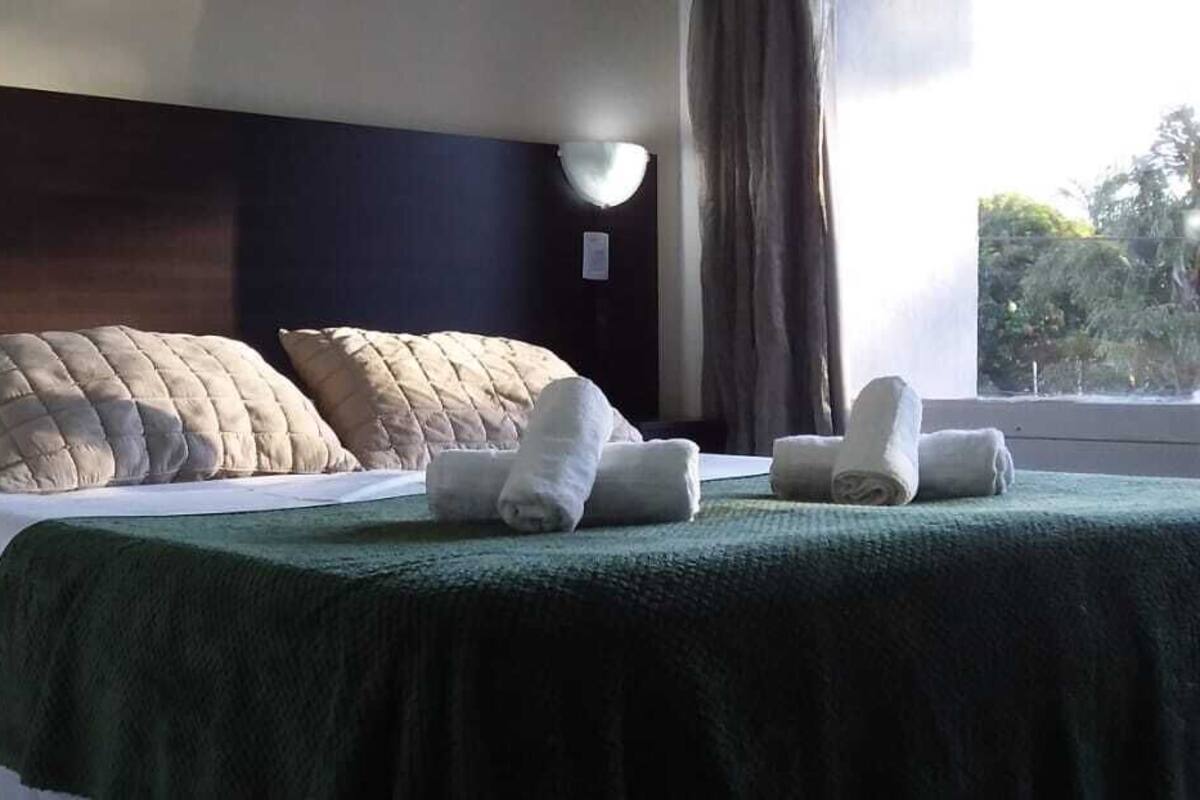 A hotel room with a bed, pillows, a green blanket, and towels.