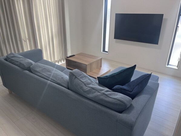 A modern living room with a grey sofa, a wooden coffee table, and a flat-screen TV mounted on the wall.