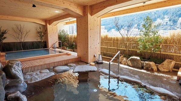Un espace de détente en bois doté d’un bain à remous, de sièges en pierre et offrant une vue sur un paysage montagneux.