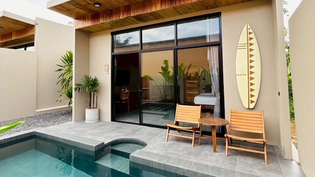 Una casa moderna con piscina, techo de madera y una tabla de surf en la pared.