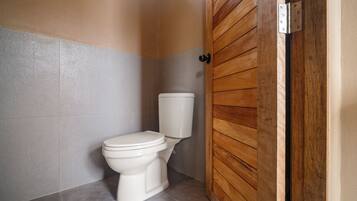 A bathroom with a white toilet, a wooden door, and a grey tiled floor.