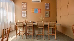 Un comedor con cuatro sillas de mimbre, una mesa larga y decoración en la pared.