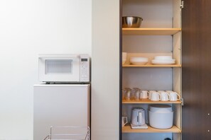 Eine Küchenzeile mit einer Mikrowelle, einem kleinen Kühlschrank, Regalen mit Geschirr, Tassen und einer Kaffeemaschine.