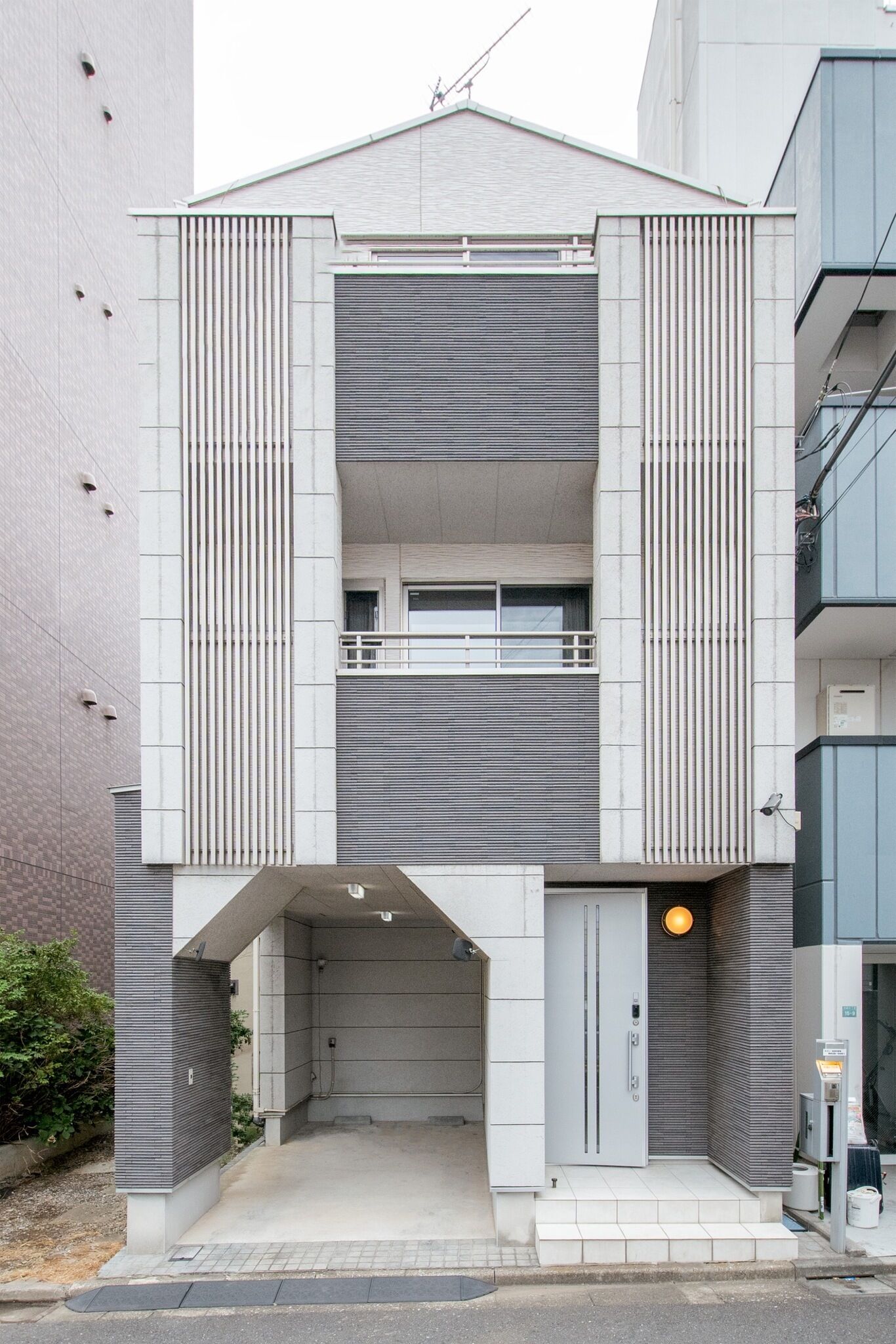 A modern building with a central entrance, two balconies, and a covered area.