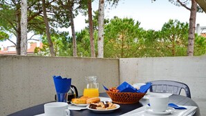 Una mesa al aire libre con comida para el desayuno, una cafetera y una cesta de pasteles.