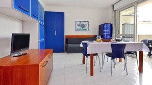 Una habitación de hotel moderna con un escritorio de madera, un televisor de pantalla plana, una zona de comedor con mesa y sillas, un armario azul y un ventanal con vistas.