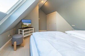 Een slaapkamer met een schuine kap, een bed, een televisie op een standaard, een kledingkast en een klein krukje.