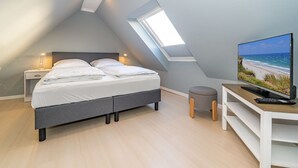 Une chambre à coucher moderne avec un lit, des lampes de chevet, une télévision et un petit tabouret.