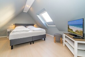 A modern bedroom with a bed, bedside lamps, a TV, and a small stool. - Lachmöwe - Holiday home in Tinnum with fireplace and terrace. (Sylt / OT Tinnum)