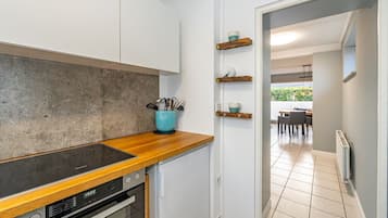 Eine moderne Küche mit weißen Schränken, einer Holzarbeitsplatte und einem eingebauten Backofen. Darüber befinden sich Regale mit Küchenutensilien.