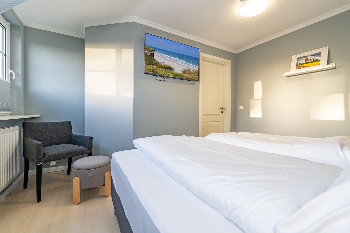 Ein Schlafzimmer mit einem Bett, einem Sessel, einem kleinen Hocker, einem Fernseher und einer Tür.