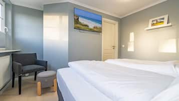 Ein Schlafzimmer mit einem Bett, einem Sessel, einem kleinen Hocker, einem Fernseher und einer Tür.