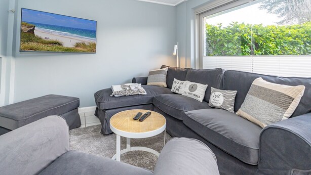 Un salon moderne avec un canapé d’angle gris, une petite table basse ronde et une photographie encadrée de plage accrochée au mur.