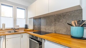 Une cuisine moderne avec des armoires blanches, un plan de travail en bois, un four encastré et une casserole bleue posée sur le plan de travail.