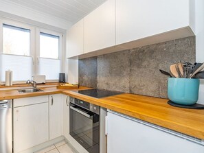 A modern kitchen with white cabinets, a wooden countertop, a built-in oven, and a blue pot on the counter.