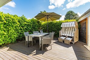 A wooden deck with a table and chairs, a striped outdoor seating area, and a large umbrella.