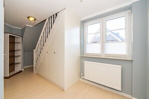Een trap met een witte leuning, een radiator onder een raam, en een houten boekenkast aan de linkerkant.