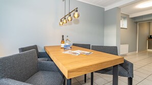 Un espace de salle à manger moderne avec une table en bois, des chaises à revêtement gris et un luminaire suspendu.