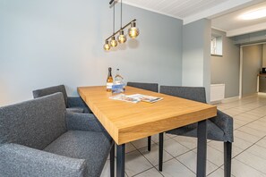 A modern dining area with a wooden table, grey upholstered chairs, and a hanging light fixture.
