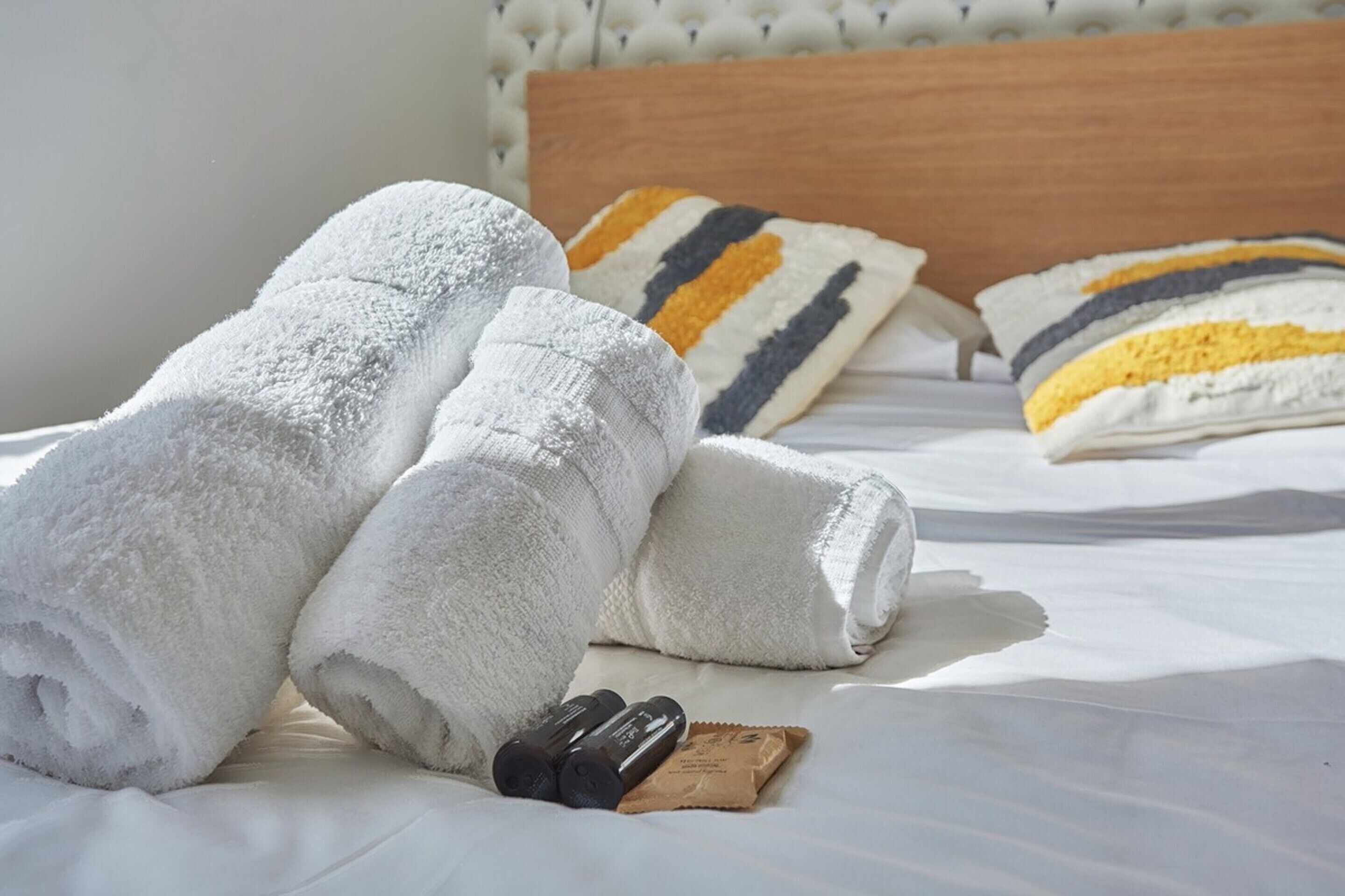 A neatly made bed with white towels, a wooden headboard, and striped pillows.