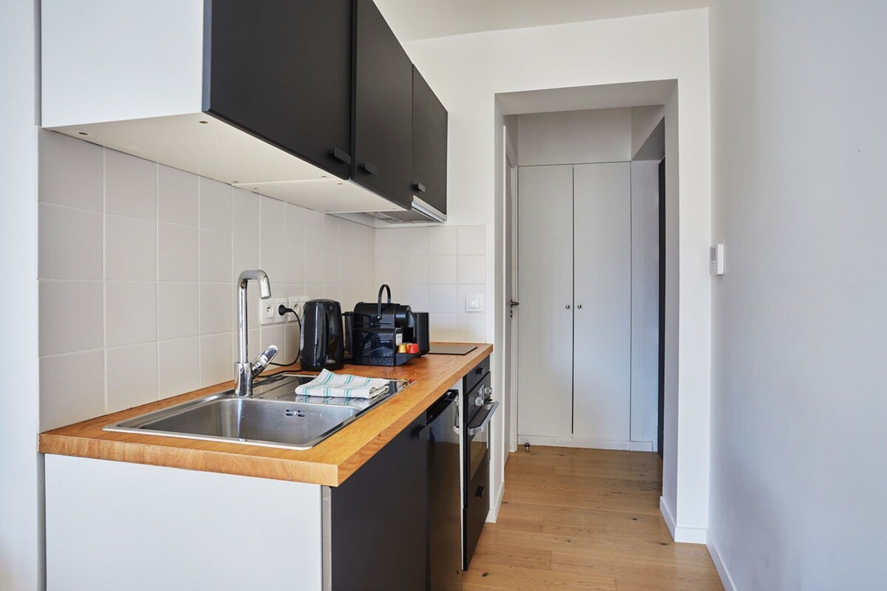 A modern kitchen with a wooden countertop, stainless steel sink, and black cabinets.