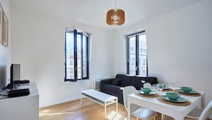 Un espacio habitable moderno con comedor, un sofá, un banco y una mesa preparada para dos.